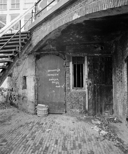 855387 Gezicht op de toegangsdeur van een werfkelder onder Geertebrug over de Oudegracht te Utrecht, aan de westzijde ...